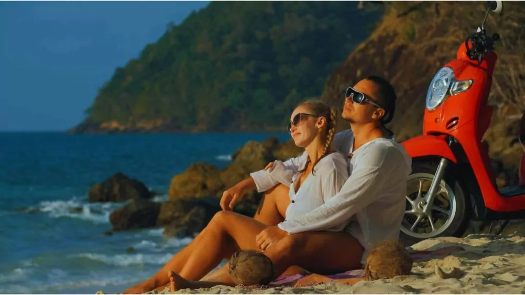 Scooter road trip. Lovely couple on red motorbike in white clothes on sand beach