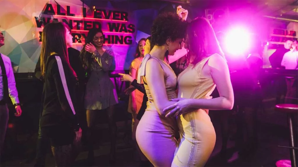 Two women dancing closely in a vibrant nightclub with neon lighting