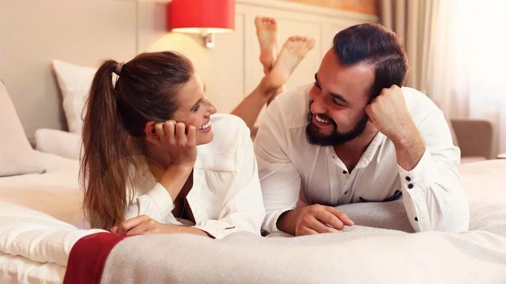 Couple lying on a bed, smiling at each other.