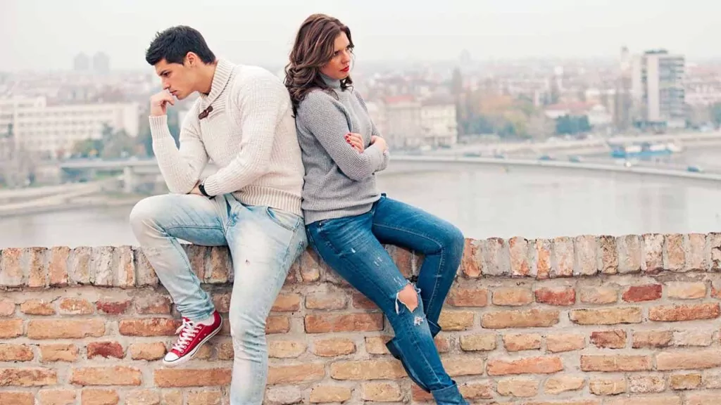 Couple sitting back to back on a brick wall, both looking frustrated and distant