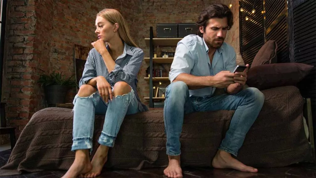 Couple sitting apart on a couch, both looking upset and disconnected