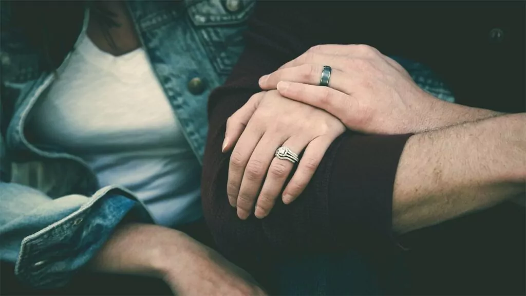 Close-up of a couple holding hands, both wearing rings, showing love and commitment