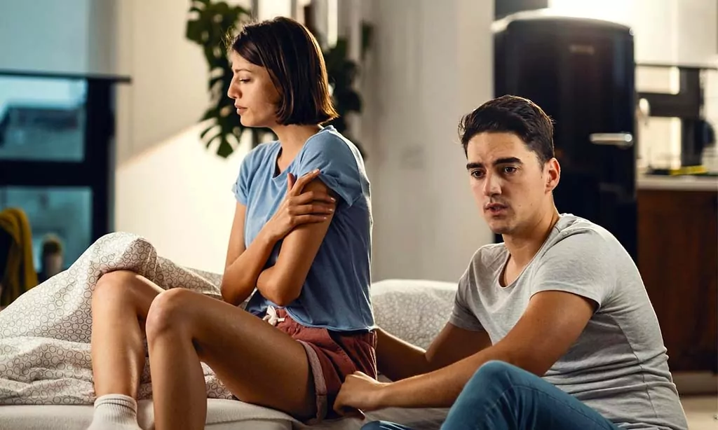 A couple appears upset, sitting on the bed and in the middle of a serious conversation