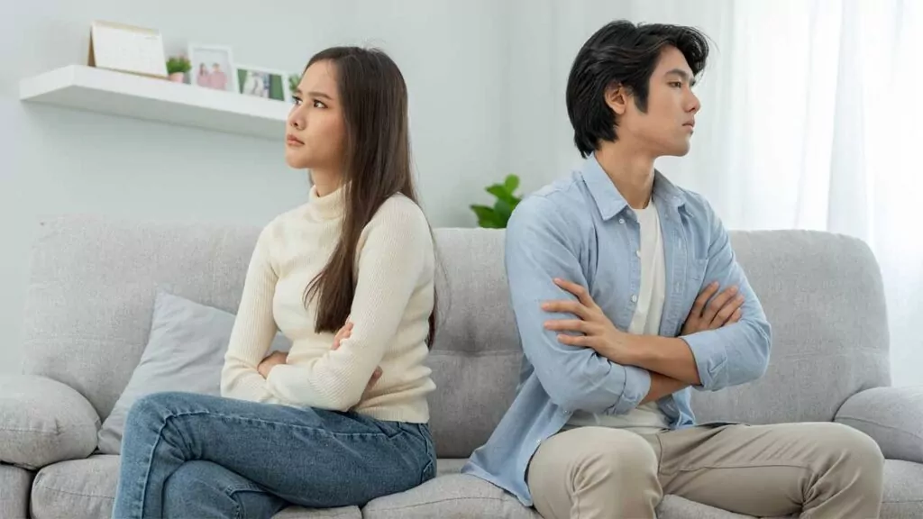 Couple sitting back to back on a couch after an argument, arms crossed