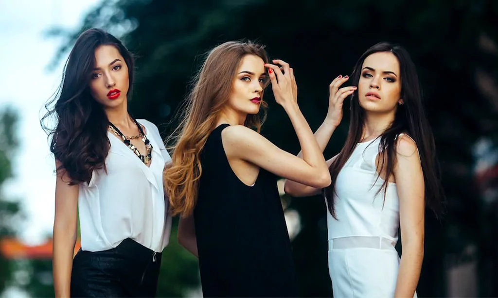 Three fashionable young women posing confidently outdoors, dressed in chic black and white outfits